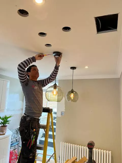 An electrician on a ladder fitting ceiling downlights