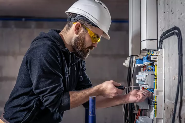 An electrician in a hard hat working at a distribution board